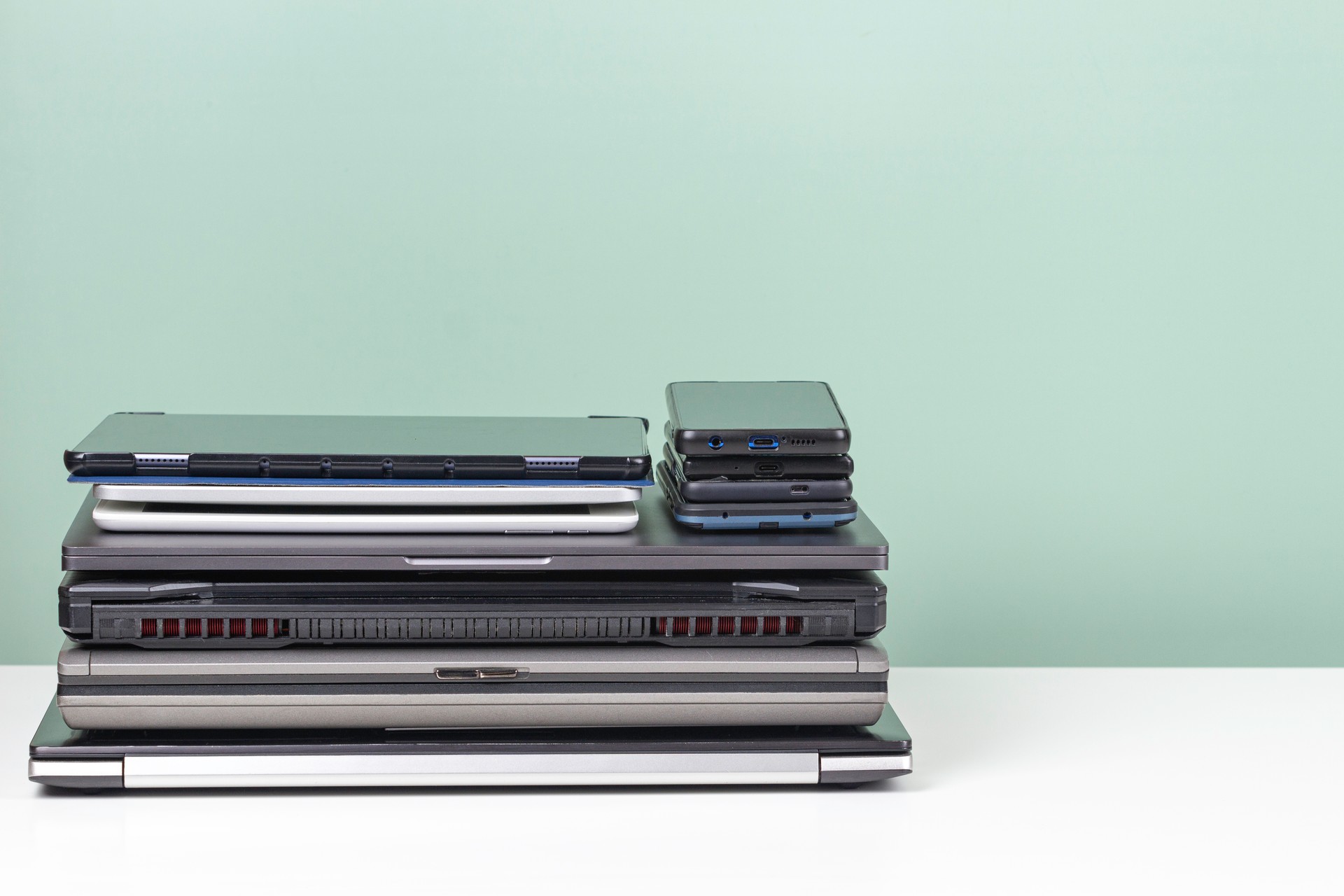 Pile of old used laptop computers, digital tablets, smartphones for recycling on white table. Planned obsolescence, e-waste, electronic waste for reuse and recycle concept